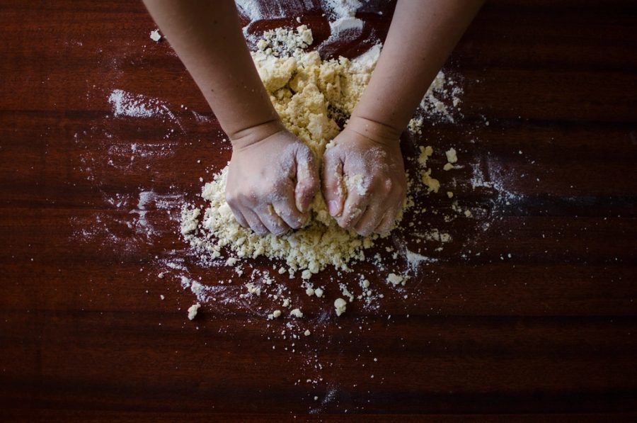 Massa de pizza sendo aberta na bancada, com os ingredientes ao lado
